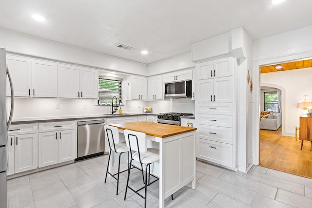 kitchen featuring appliances with stainless steel finishes, a sink, butcher block countertops, a kitchen bar, and visible vents