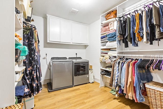 clothes washing area featuring light wood-style floors, washing machine and dryer, and cabinet space
