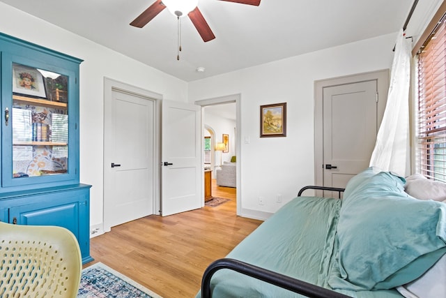 bedroom featuring arched walkways, baseboards, ceiling fan, and light wood-style flooring