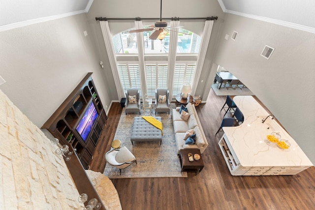 living room featuring crown molding, a ceiling fan, wood finished floors, a towering ceiling, and visible vents