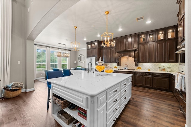kitchen with dark brown cabinetry, an inviting chandelier, decorative backsplash, stainless steel gas stovetop, and visible vents