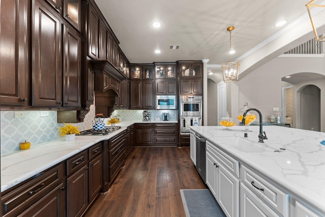 kitchen featuring appliances with stainless steel finishes, arched walkways, dark brown cabinets, a sink, and glass insert cabinets