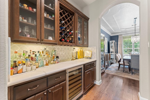 bar featuring beverage cooler, arched walkways, wet bar, wood finished floors, and tasteful backsplash