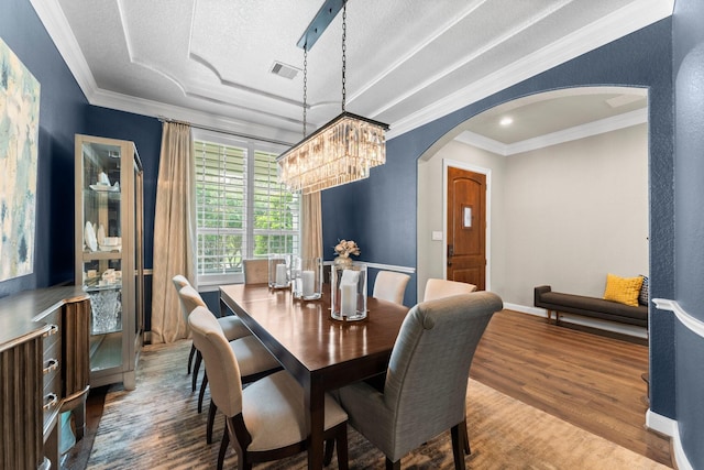dining room featuring crown molding, arched walkways, wood finished floors, and visible vents