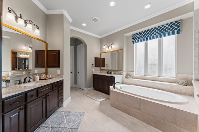 full bathroom with a sink, two vanities, visible vents, ornamental molding, and a garden tub