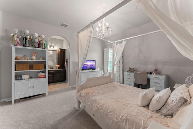 bedroom with connected bathroom, visible vents, arched walkways, a notable chandelier, and light carpet