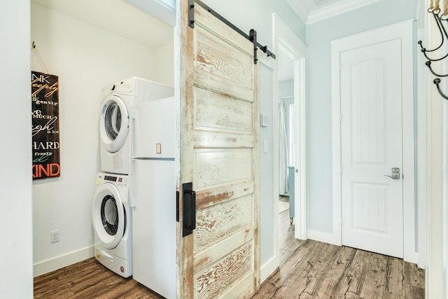 laundry room with stacked washer / drying machine, a barn door, wood finished floors, baseboards, and ornamental molding