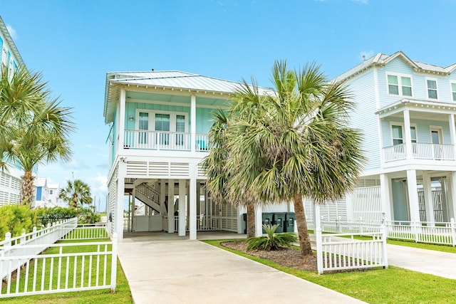 coastal home with fence, covered porch, stairs, driveway, and a carport