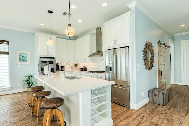 kitchen featuring visible vents, crown molding, wall chimney range hood, a sink, and appliances with stainless steel finishes