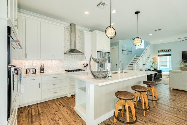 kitchen featuring a sink, wall chimney exhaust hood, stainless steel appliances, tasteful backsplash, and visible vents