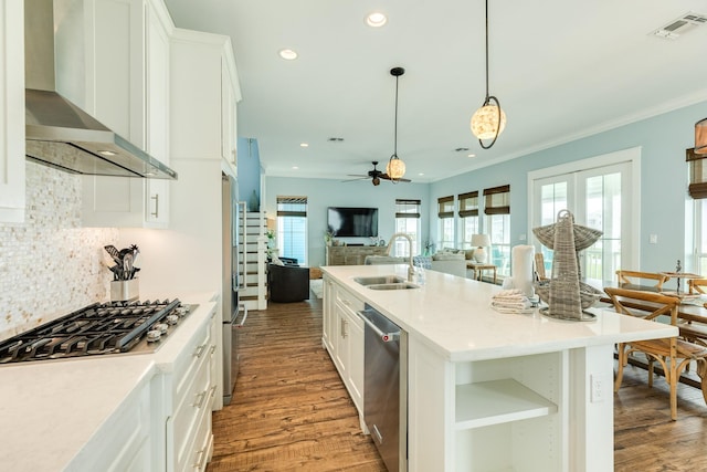kitchen featuring open floor plan, light wood-type flooring, wall chimney exhaust hood, a sink, and stainless steel appliances