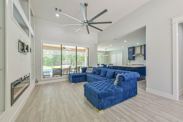 living area with baseboards, ceiling fan, light wood finished floors, and a towering ceiling
