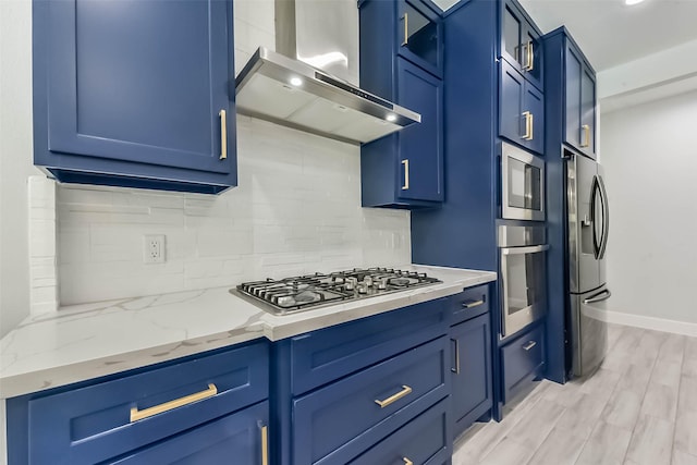 kitchen featuring decorative backsplash, blue cabinetry, appliances with stainless steel finishes, light wood-type flooring, and wall chimney exhaust hood