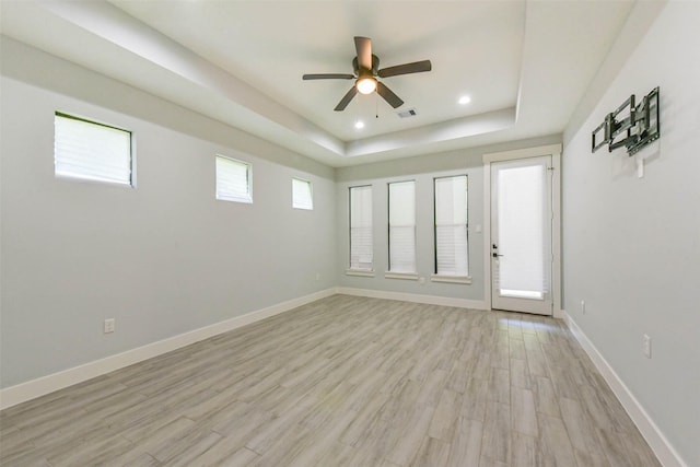 spare room featuring a raised ceiling, light wood-style floors, a ceiling fan, baseboards, and visible vents