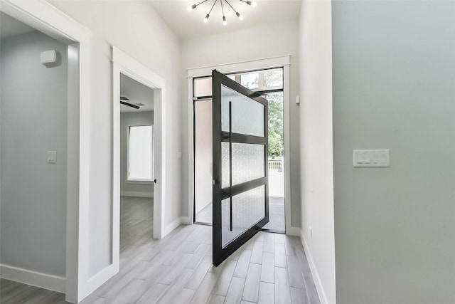 foyer with baseboards, an inviting chandelier, and light wood-style flooring