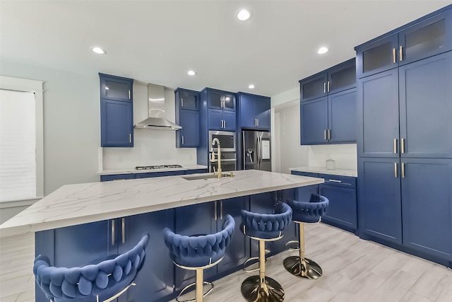 kitchen with wall chimney range hood, a kitchen breakfast bar, blue cabinetry, and appliances with stainless steel finishes