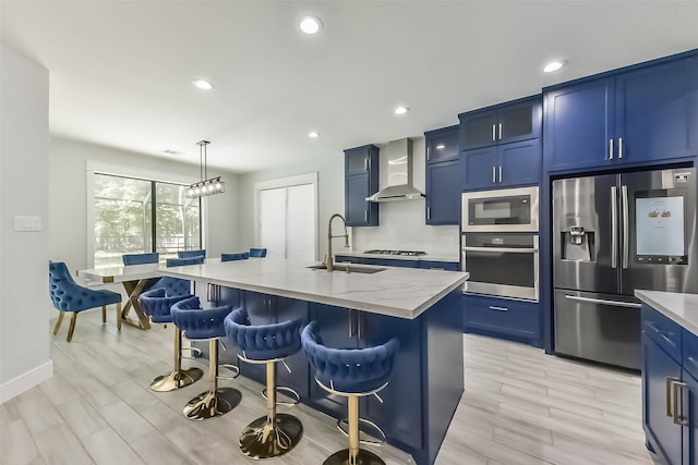 kitchen featuring wall chimney range hood, appliances with stainless steel finishes, a breakfast bar, a sink, and blue cabinetry