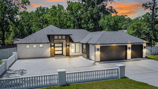 prairie-style home featuring fence private yard, a garage, roof with shingles, and driveway