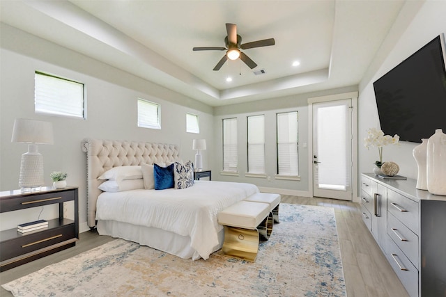 bedroom with access to outside, visible vents, a raised ceiling, and light wood-type flooring