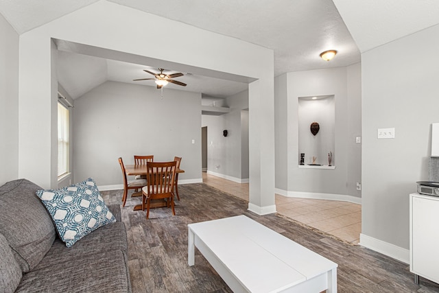 living area featuring a ceiling fan, baseboards, vaulted ceiling, and wood finished floors