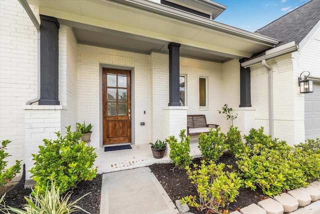 doorway to property with covered porch, an attached garage, and brick siding