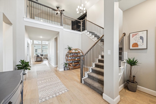 stairway with baseboards, a high ceiling, wood finished floors, and a notable chandelier