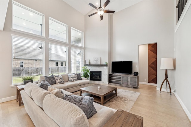 living area with light wood-style floors, baseboards, ceiling fan, and high vaulted ceiling