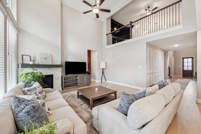 living room with a ceiling fan, a high ceiling, baseboards, and a fireplace