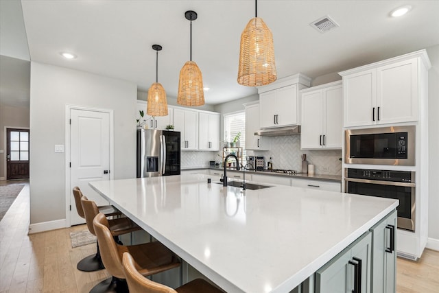 kitchen with a sink, light wood finished floors, tasteful backsplash, and stainless steel appliances