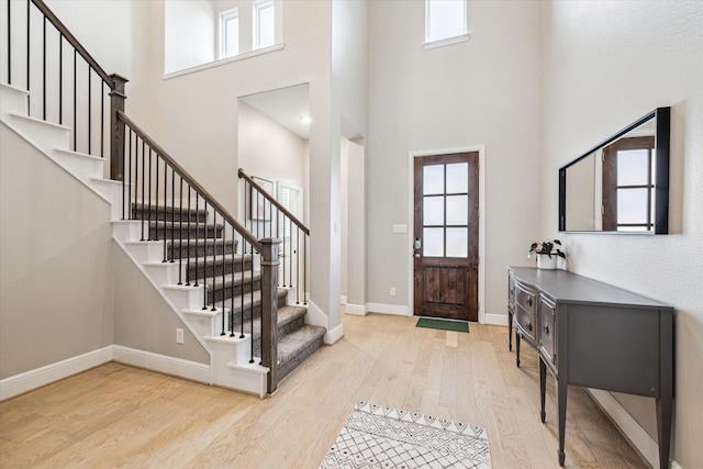 foyer featuring a healthy amount of sunlight, baseboards, a high ceiling, and wood finished floors