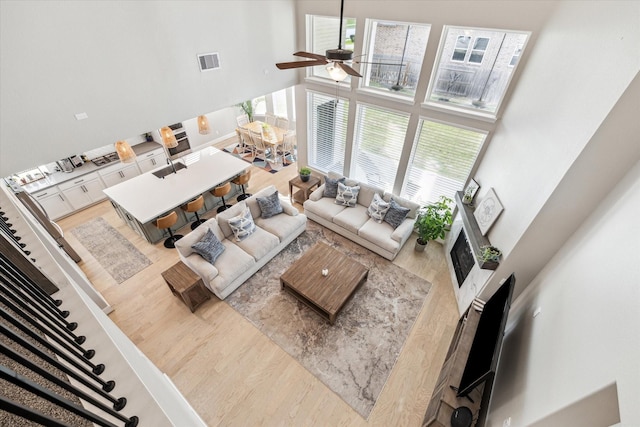 living room with a high ceiling, a ceiling fan, a wealth of natural light, wood finished floors, and visible vents