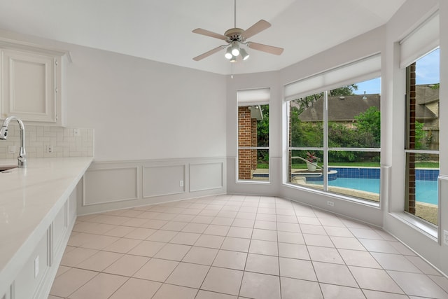 unfurnished dining area with a sink, wainscoting, ceiling fan, and light tile patterned floors