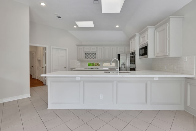 kitchen with appliances with stainless steel finishes, a sink, vaulted ceiling with skylight, light countertops, and tasteful backsplash