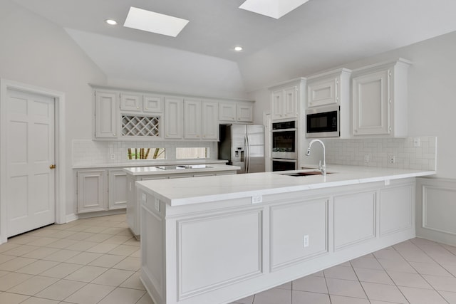 kitchen with vaulted ceiling with skylight, backsplash, appliances with stainless steel finishes, light countertops, and a peninsula