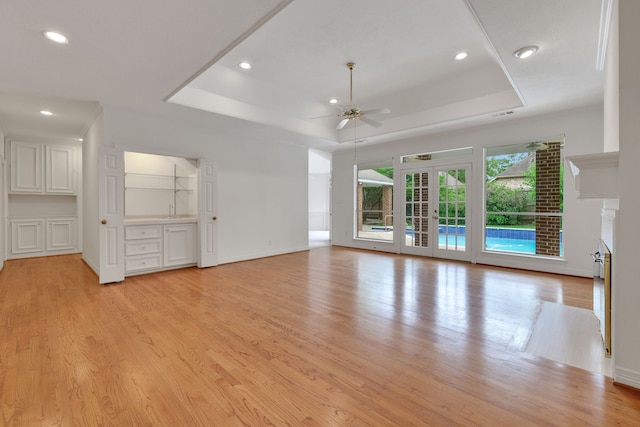 unfurnished living room featuring a tray ceiling, ceiling fan, and light wood-style floors