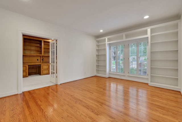 empty room with crown molding, baseboards, light wood-type flooring, built in desk, and built in shelves