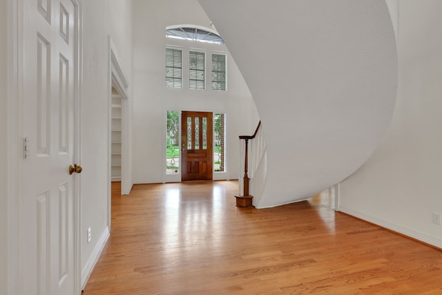entrance foyer with a towering ceiling, baseboards, and light wood-style floors