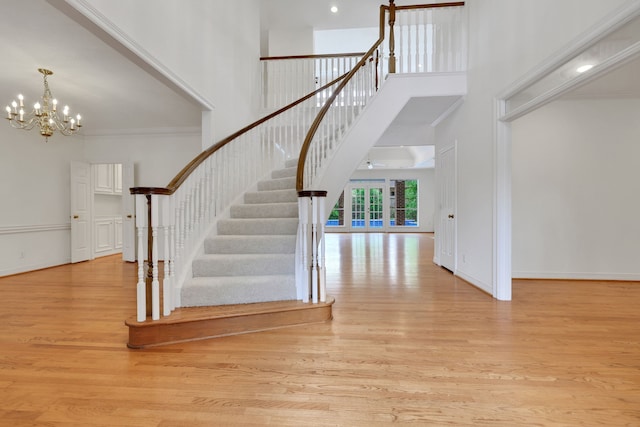 stairs featuring ornamental molding, a towering ceiling, wood finished floors, baseboards, and a notable chandelier