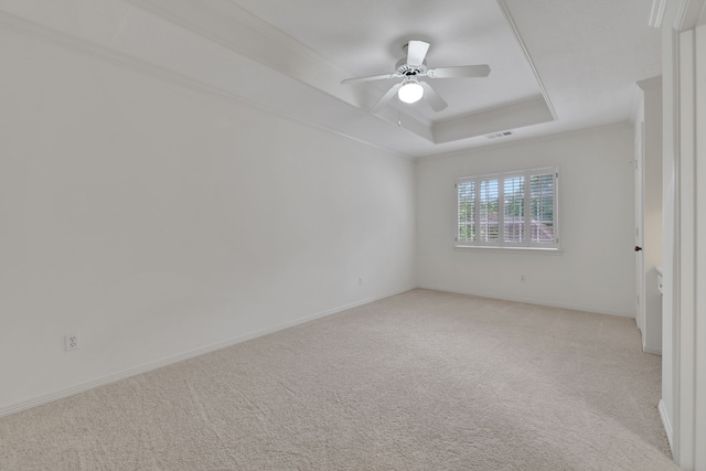 empty room featuring a raised ceiling, ceiling fan, light carpet, and visible vents