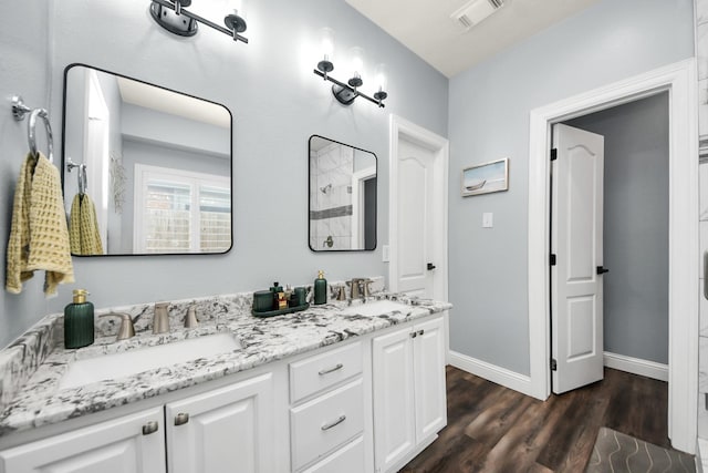 full bathroom with a sink, double vanity, wood finished floors, and visible vents