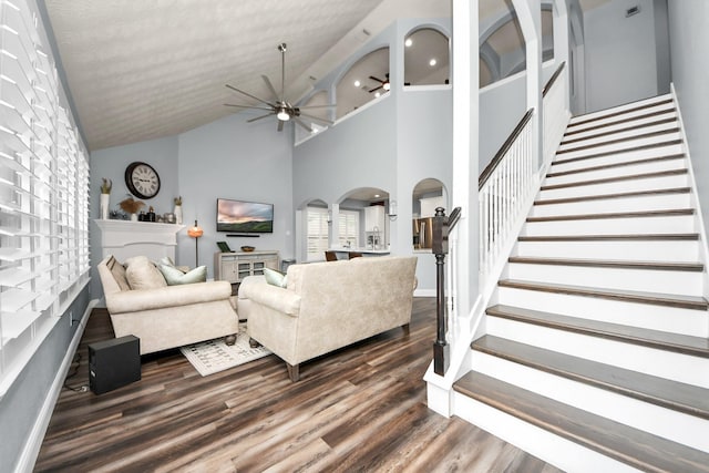 living area with arched walkways, high vaulted ceiling, a ceiling fan, dark wood-type flooring, and stairway