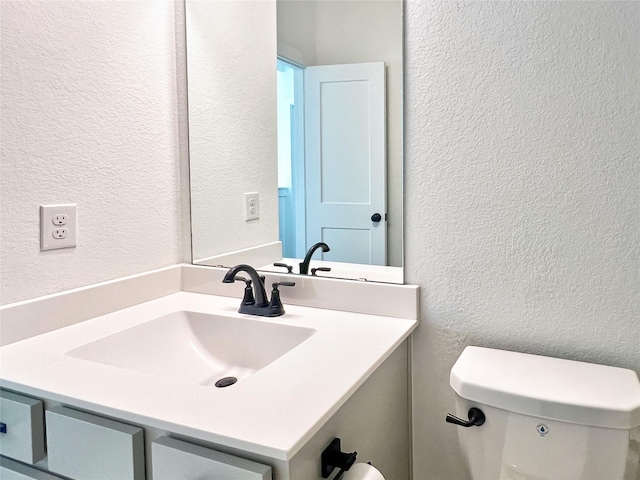 half bath with vanity, a textured wall, and toilet