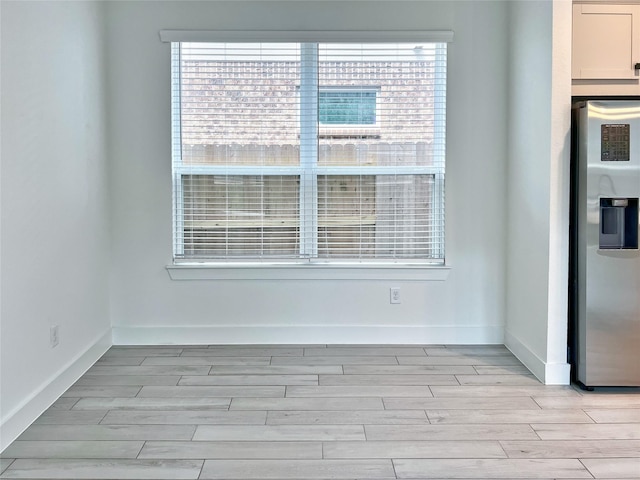 unfurnished dining area with baseboards, a healthy amount of sunlight, and light wood-style flooring