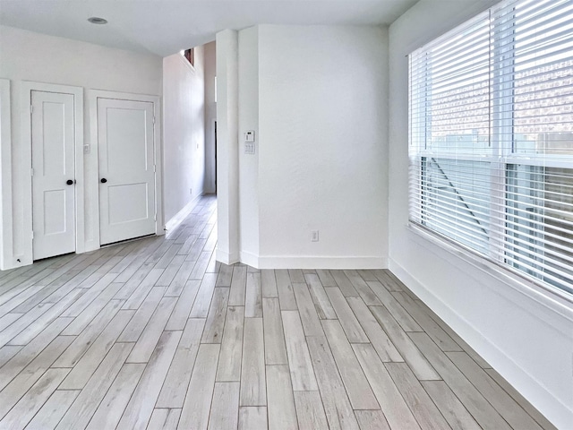 unfurnished room featuring baseboards, light wood-style flooring, and a wealth of natural light