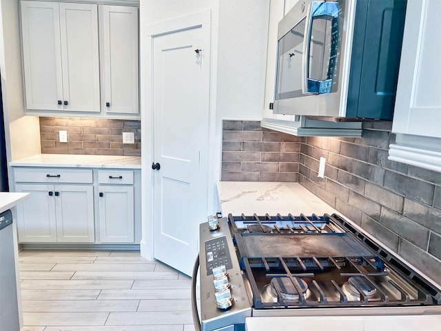kitchen featuring appliances with stainless steel finishes, tasteful backsplash, light stone countertops, and light wood finished floors