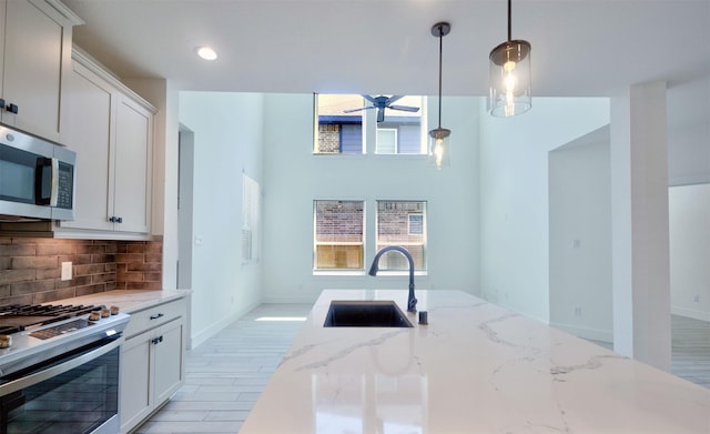 kitchen with decorative backsplash, a ceiling fan, appliances with stainless steel finishes, hanging light fixtures, and a sink