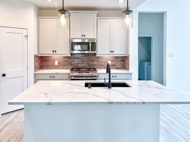 kitchen with backsplash, appliances with stainless steel finishes, a center island with sink, a sink, and washer and dryer