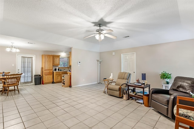 living area with a textured ceiling, ceiling fan with notable chandelier, baseboards, light tile patterned floors, and visible vents
