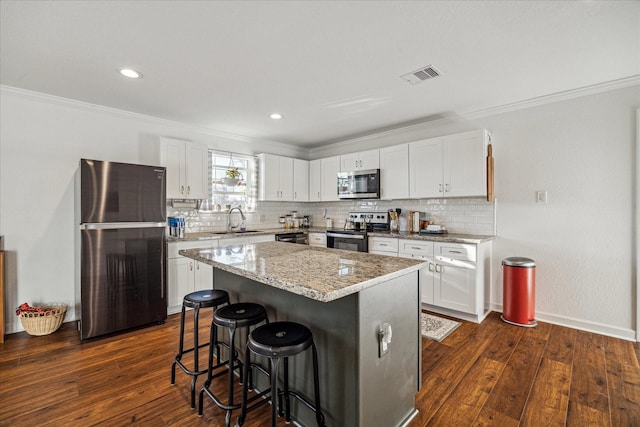 kitchen with a breakfast bar area, backsplash, appliances with stainless steel finishes, a sink, and ornamental molding