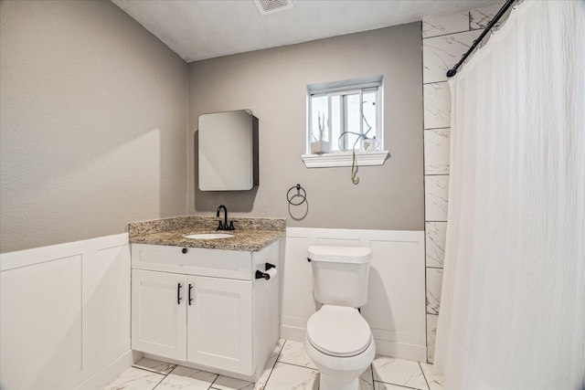 full bath featuring wainscoting, vanity, toilet, marble finish floor, and a decorative wall